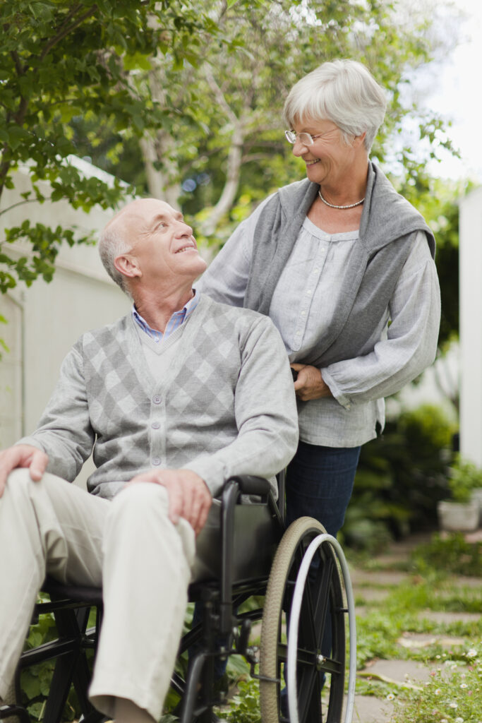 Elderly man sits in a wheelchair and smiles at the woman behind him pushing the chair