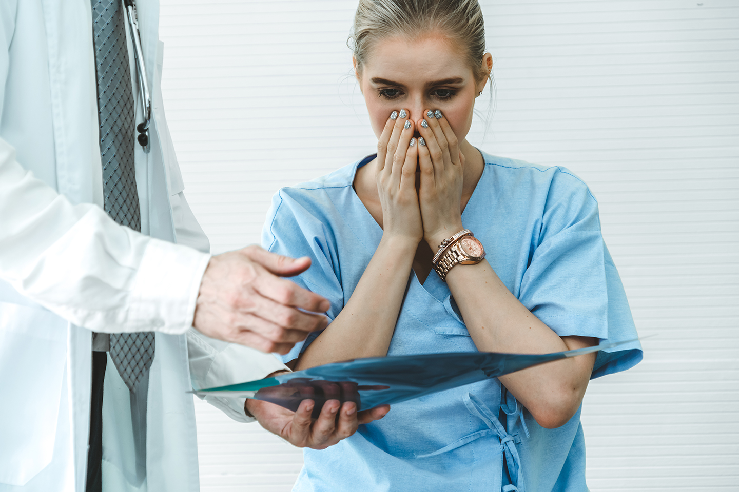 Woman in hospital gown with hands covering mouth shocked at what the doctor is showing her