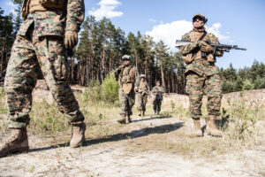 Location shot of United States Marine with rifle weapons in uniforms. Military equipment, army helmet, warpaint, smoked dirty face, tactical gloves. Military action, battlefield