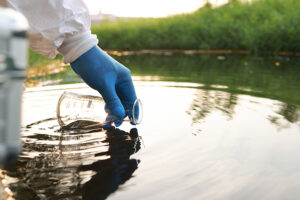 Gloved hand extracts a water sample from a body of water