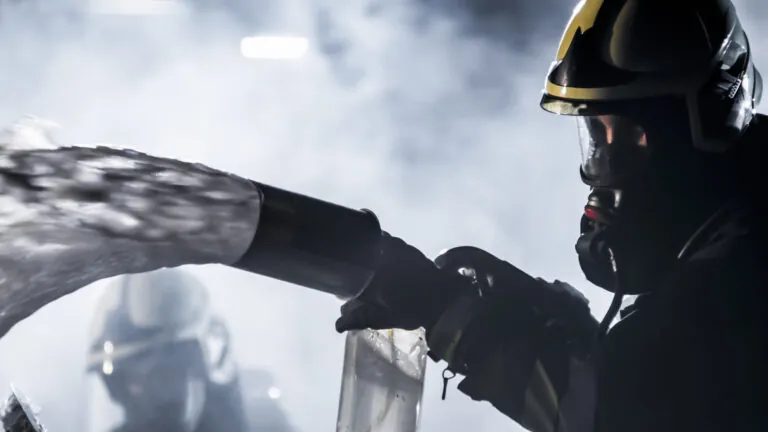 Firefighter in silhouette spraying foam from a hose