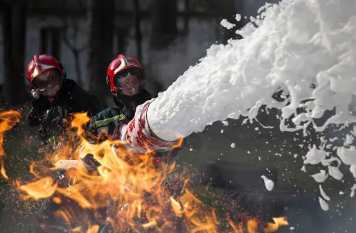 firefighters extinguish flames with foam from a large hose