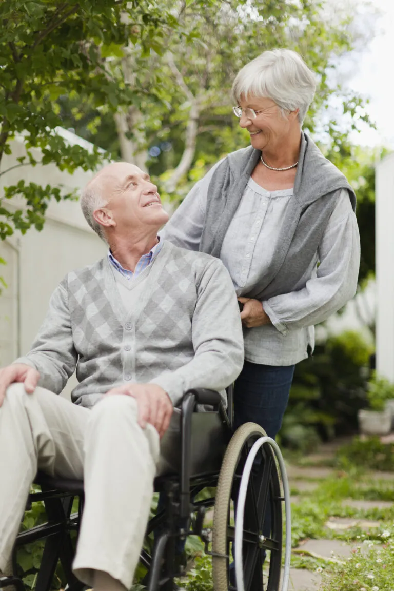 Elderly man sits in a wheelchair and smiles at the woman behind him pushing the chair